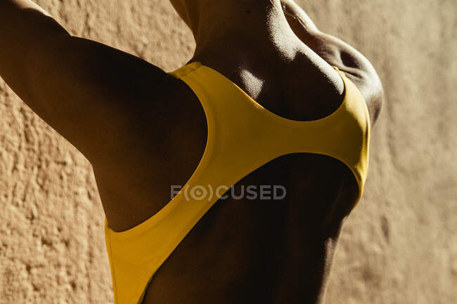 Back view of young woman back in yellow swimwear against yellow wall — Stock Photo
