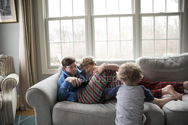 Irmão adolescente com gripe joga Ipad, Little Brothers Watch — Fotografia de Stock