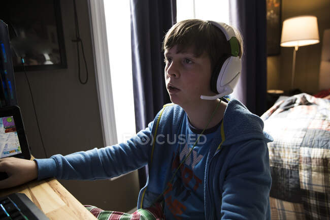 Primer plano de adolescente chico usando auriculares jugando juego de ordenador - foto de stock