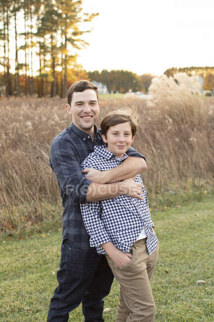 Older Cousin Embraces Teen Cousin During Sunset in Front of Field — Stock Photo