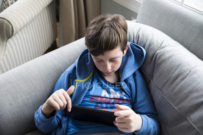 Vista aérea brillante de adolescente con gripe sentado en el sofá viendo Ipad - foto de stock