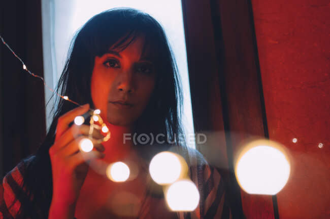 Sério jovem mulher olhando através das luzes coloridas — Fotografia de Stock