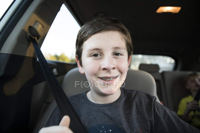Primer plano de sonriente adolescente chico con frenos sentado en el coche - foto de stock