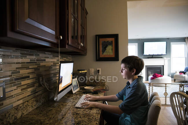 Широкий вид мальчика-близнеца, сидящего на клавиатуре за рабочим столом — стоковое фото