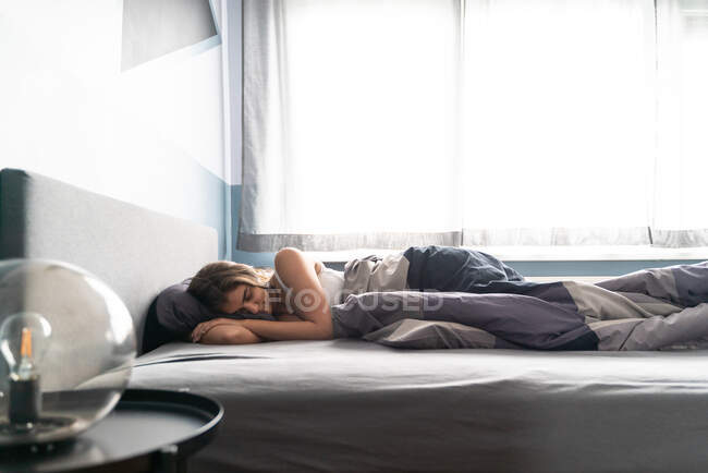 Establishing shot of a young woman sleeping peacefully at her room on the bed during the morning light. — Stock Photo