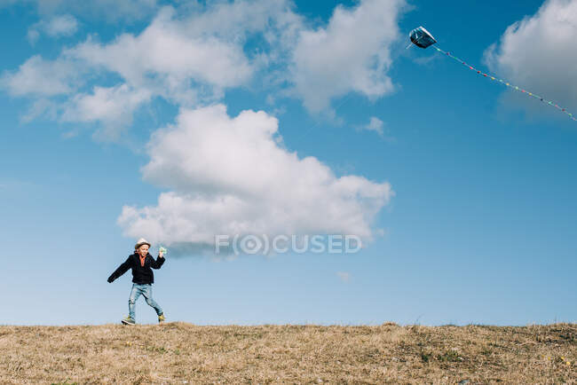 Jeune garçon volant un cerf-volant sur le sommet d'une colline par une belle journée — Photo de stock