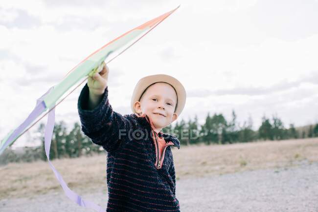Мальчик держит воздушного змея, улыбающегося на улице в солнечный день — стоковое фото