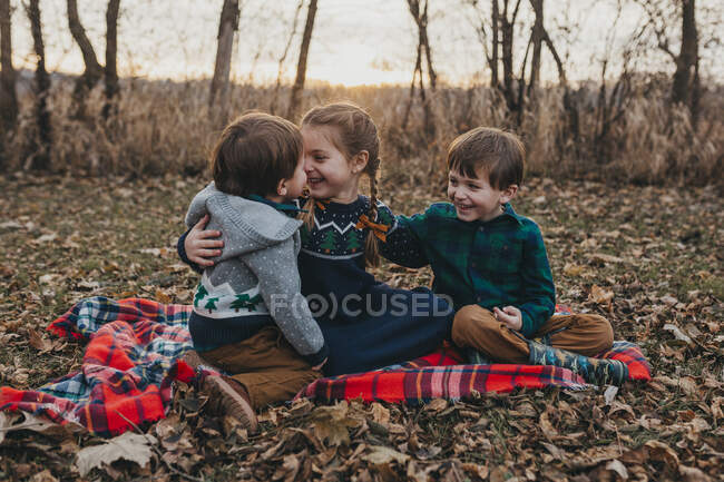 Троє братів і сестер сидять на червоній ковдрі, сміючись. — стокове фото