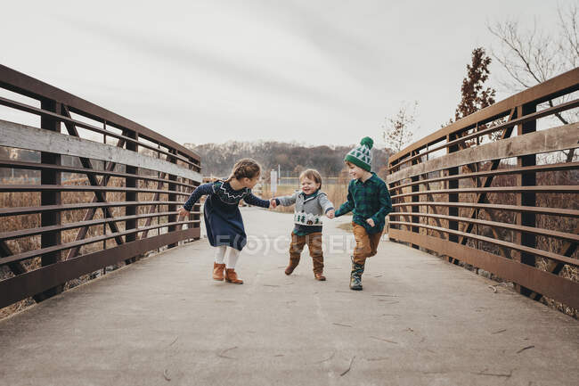 Tre fratelli che ridono tenendosi per mano correndo sul ponte — Foto stock
