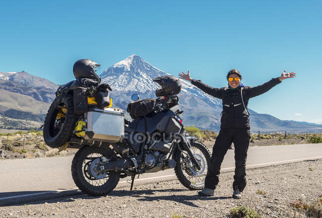 Mulher de pé ao lado de uma moto de turismo. Vulcão Lanin na parte de trás — Fotografia de Stock