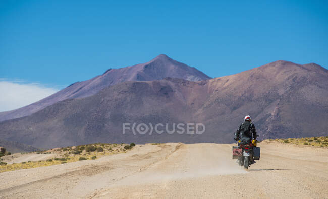 Человек едет на мотоцикле по пыльной дороге в Боливии — стоковое фото