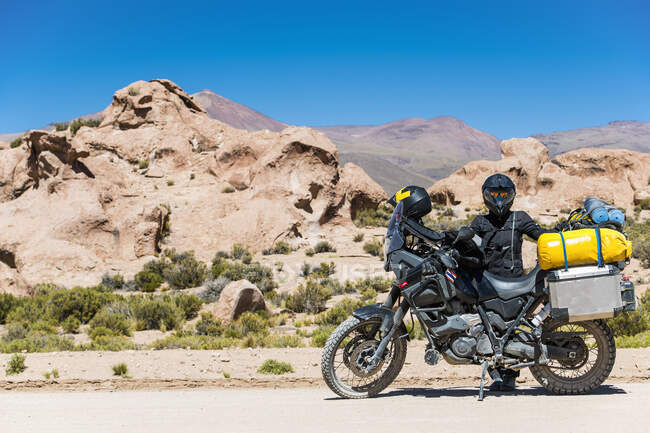 Mujer de pie junto a una motocicleta de gira en una carretera polvorienta en Bolivia - foto de stock