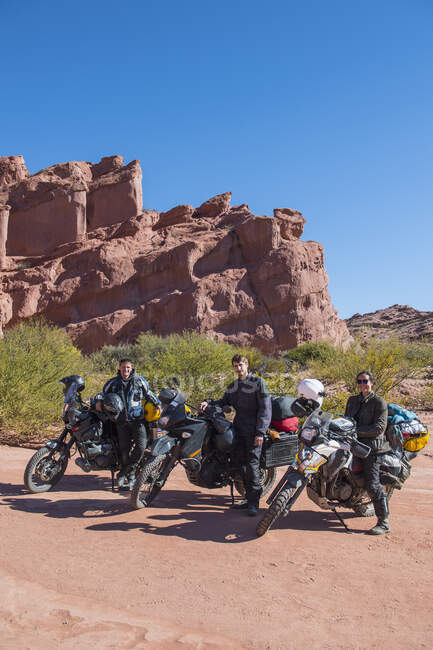 Grupo de amigos de pie junto a motocicletas de turismo en el desierto - foto de stock