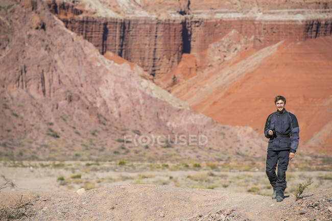 Man in motorcycle gear, standing in front of red sandstone formations — Stock Photo