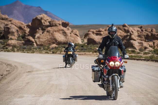 Dos amigos montando en motocicleta en carretera polvorienta en Bolivia - foto de stock