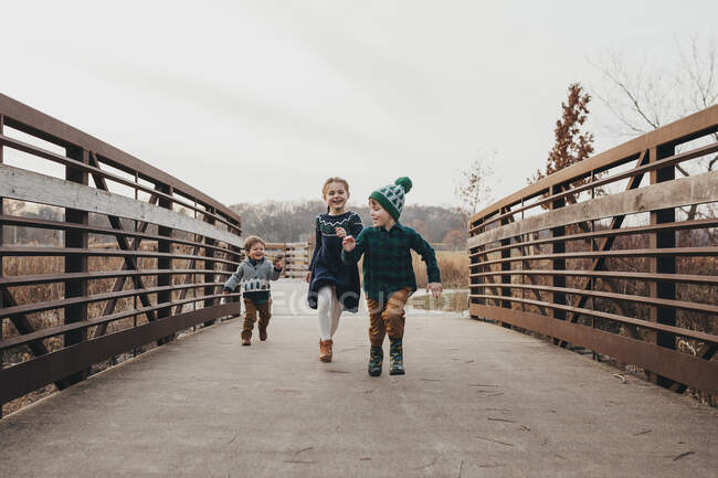 Братья и сёстры бегут вместе по мосту к камере — стоковое фото