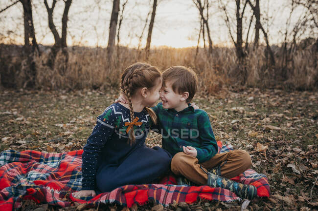 Boy and Girl Siblings smiling at each other sitting on red plaid blank — Stock Photo