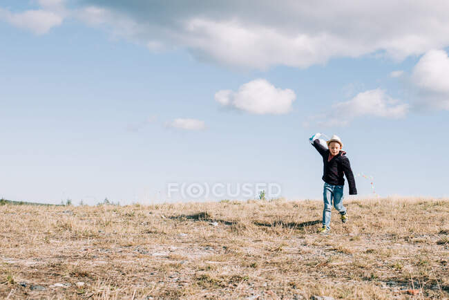 Kleiner Junge läuft an einem sonnigen Tag mit einem Drachen auf einem Hügel — Stockfoto