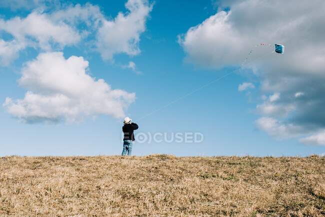 Niño volando una cometa en una colina en un hermoso día soleado - foto de stock