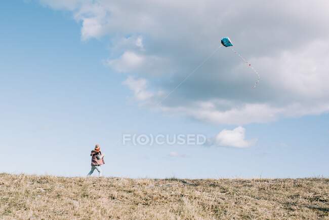 Ragazza che vola un aquilone in cima a una collina con un soffice cielo nuvoloso — Foto stock