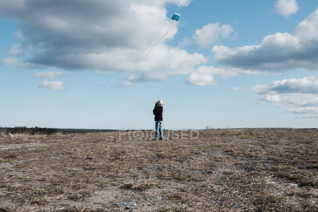 Niño volando una cometa en la cima de una colina en un día de nubes esponjosas - foto de stock