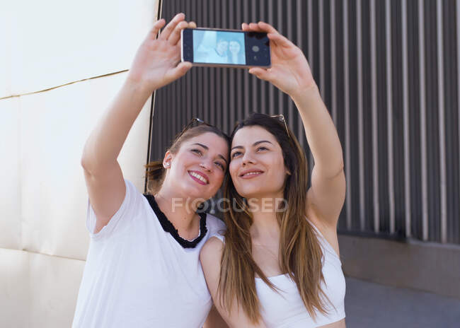 Dos amigos sostienen el teléfono en sus manos para hacer una selfie - foto de stock