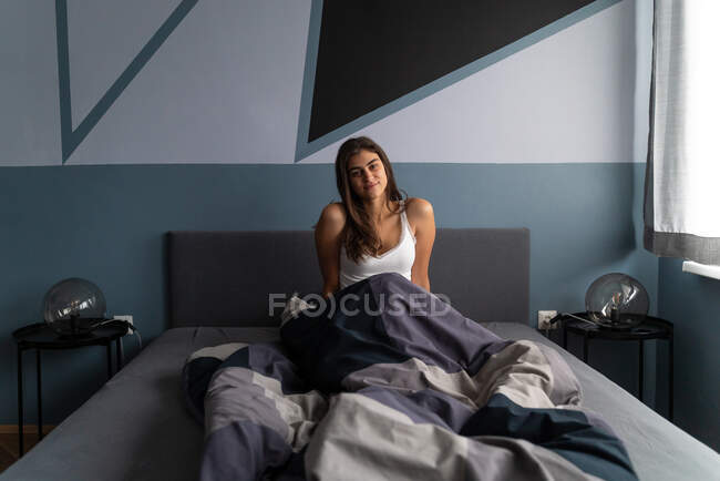 Média foto de uma mulher morena atraente sentada em sua cama durante a luz da manhã. — Fotografia de Stock