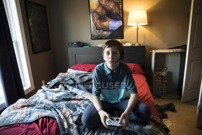 Високий вигляд підлітка Хлопчик ігри під час носіння гарнітури, сидячи на ліжку — стокове фото