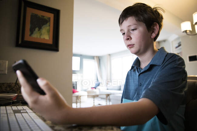 Low View of Tween Boy at Computer Desk Reading Texts on iPhone — Stock Photo
