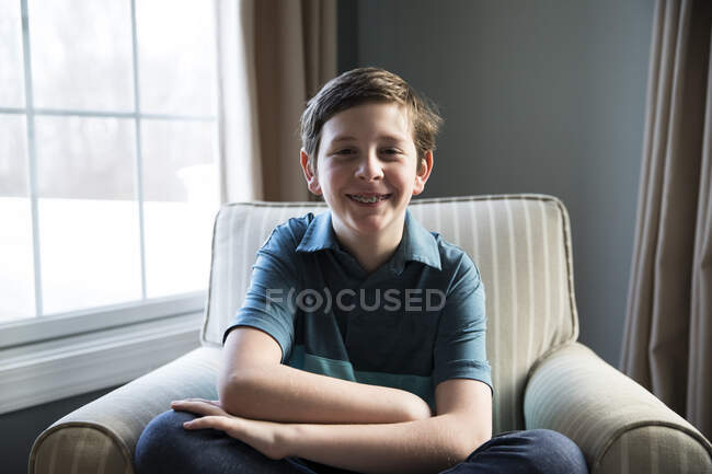 Close Up of Sorrindo Tween Boy com aparelho, sentado em cadeira listrada — Fotografia de Stock