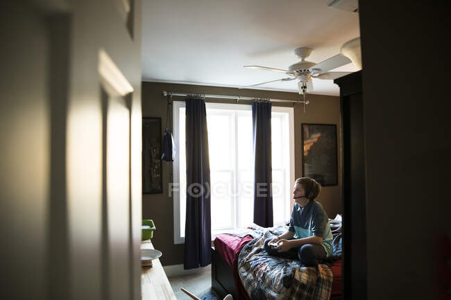 Visão ampla de jogos de adolescente enquanto usa fone de ouvido, sentado na cama — Fotografia de Stock