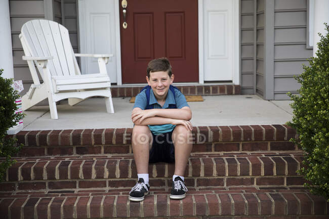 Sonriente Tween Boy con frenos se sienta en los escalones delanteros de ladrillo - foto de stock