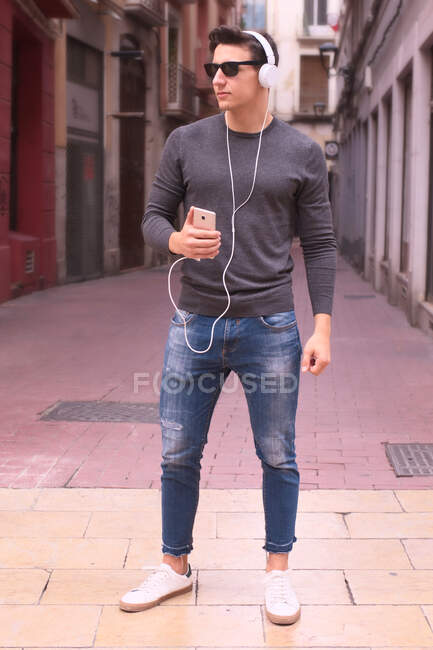 Привлекательный молодой человек слушает музыку с наушниками на улице — стоковое фото