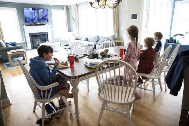 Cuatro hermanos de edad preescolar a adolescente comer pizza en la mesa desordenada - foto de stock