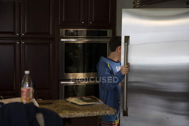 Adolescente sin rostro abre la puerta del refrigerador de acero inoxidable busca comida - foto de stock