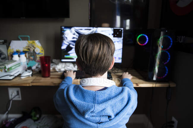 Vista trasera de adolescente chico jugando juego de ordenador en un escritorio desordenado - foto de stock