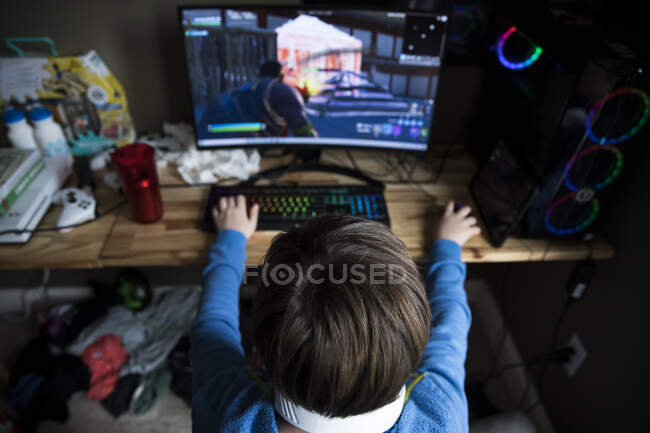 Vista alta de Teen Boy jugando en la computadora de juego en el escritorio desordenado - foto de stock