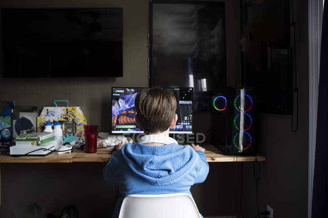 Vue arrière de adolescent garçon jouant sur l'ordinateur de jeu au bureau désordonné — Photo de stock