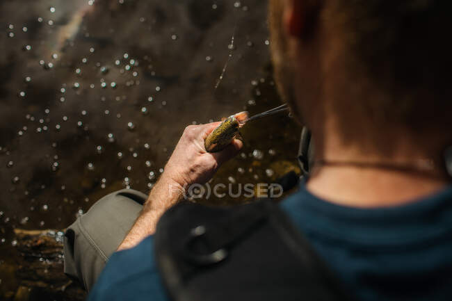 Man removes hook from the mouth of a small fish — Stock Photo