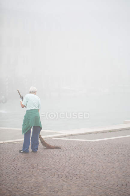 Vecchia donna che spazza durante la mattina nebbiosa, Venezia, Italia. — Foto stock