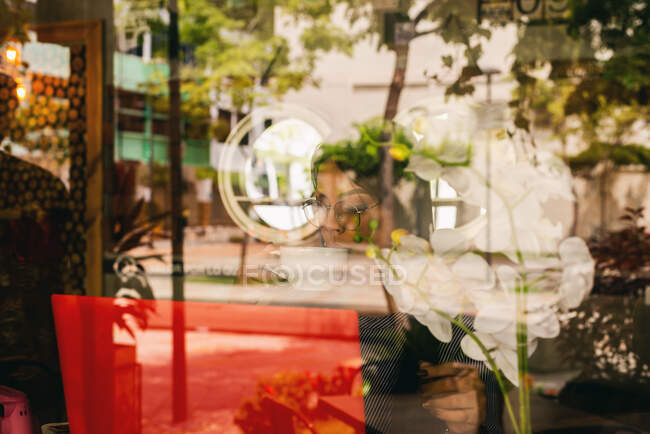 Mujer vista a través del vidrio mientras bebe café en una cafetería - foto de stock