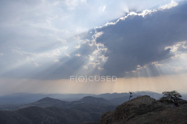 Um homem correndo descendo uma rocha sob um céu nublado com raios de sol — Fotografia de Stock