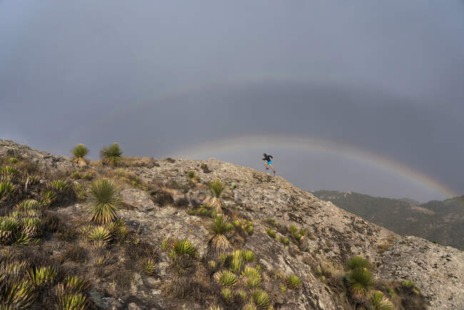 Un uomo che corre su una roccia sotto un arcobaleno — Foto stock