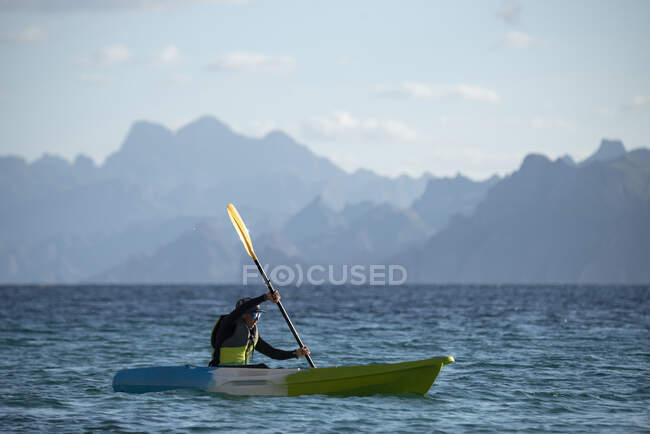 Une femme pagayant sur un siège sur le kayak supérieur près de la rive de l'île Carmen à Loreto, Basse-Californie, Mexique. — Photo de stock