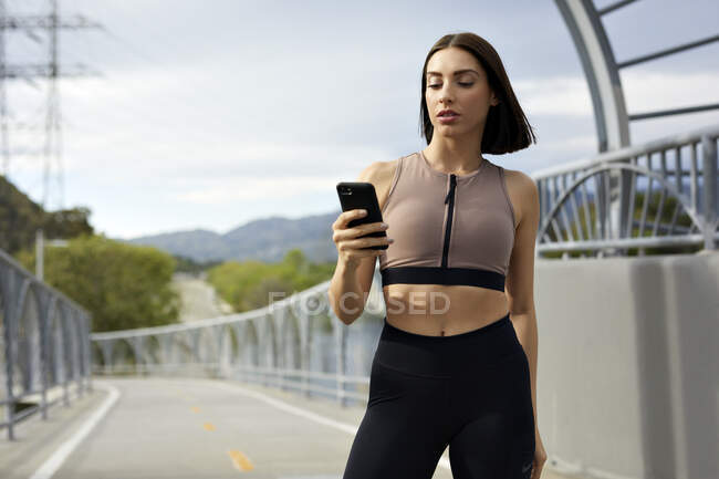 Jogger text messaging on smart phone while standing at bridge — Stock Photo