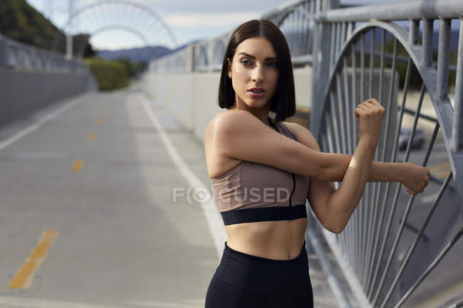 Joggerin schaut weg, während sie auf Brücke die Arme ausstreckt — Stockfoto