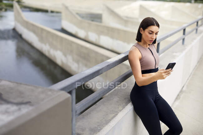 Молодая женщина с помощью мобильного телефона, стоя на мосту — стоковое фото