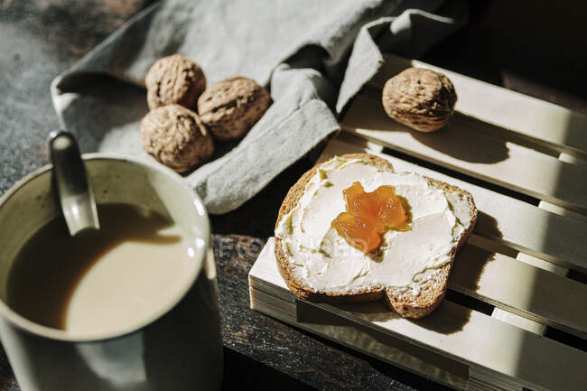 From above of tasty piece of bread with butter and jam placed on table with walnuts and fresh coffee — Stock Photo