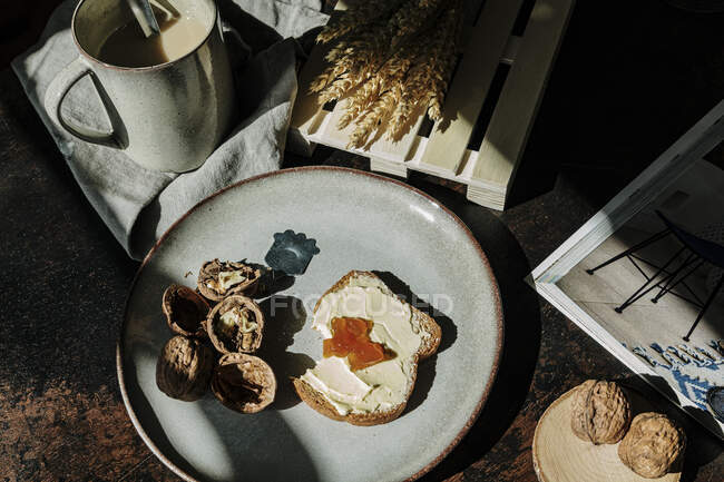 De cima de pedaço saboroso de pão com manteiga e geléia colocados na mesa com nozes e café fresco — Fotografia de Stock