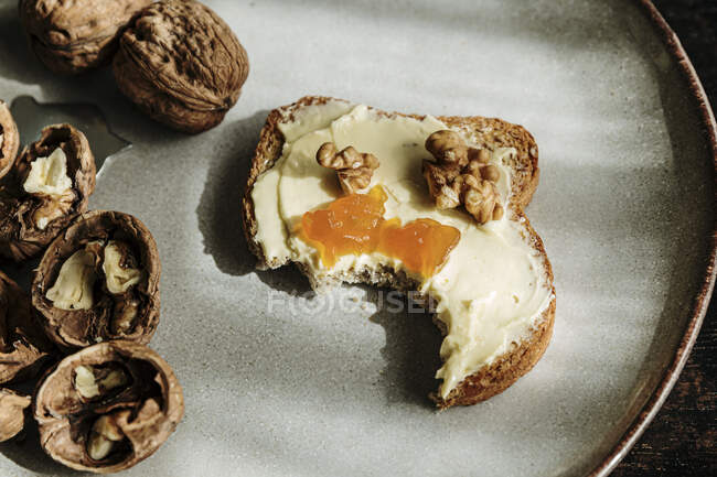 Toast with butter, jam and walnuts placed on a fancy plate on wooden board near walnuts — Stock Photo
